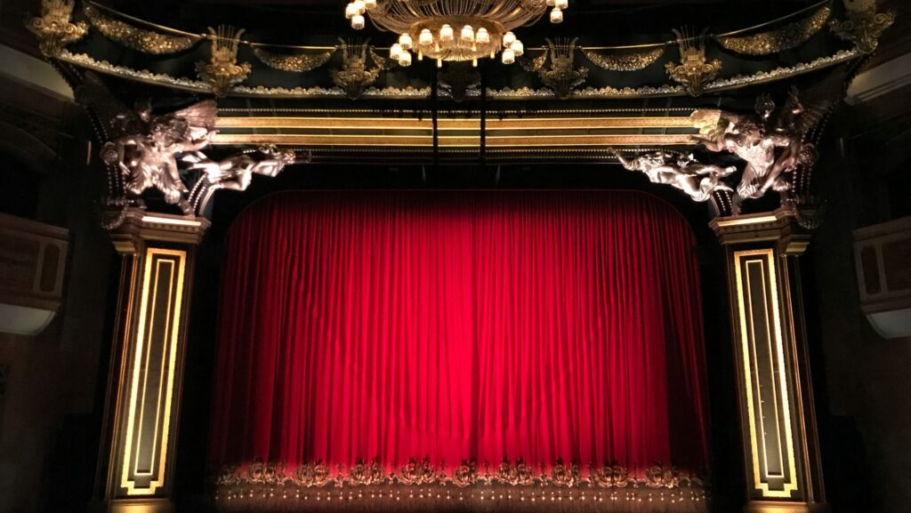 Image shows a closed red curtain on theatre stage - is the stage set for musical after musical?