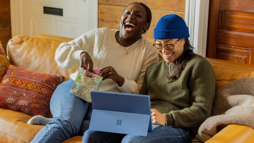 Two friends sitting on a sofa, laughing at something and looking happy and relaxed.