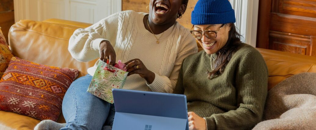 Two friends sitting on a sofa, laughing at something and looking happy and relaxed.