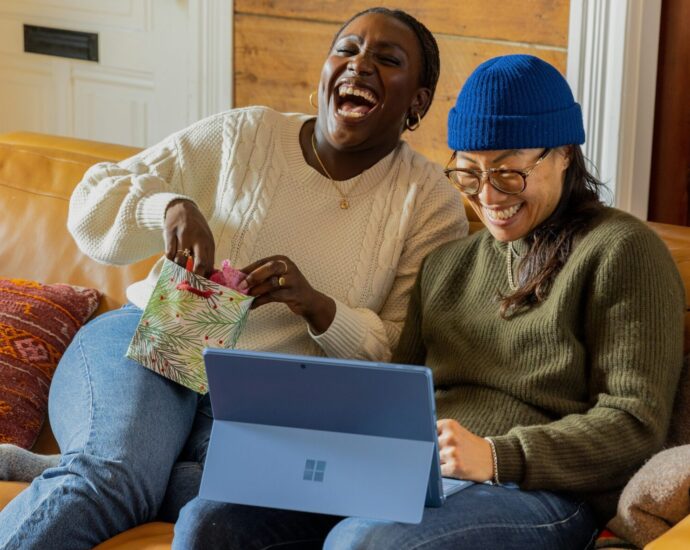 Two friends sitting on a sofa, laughing at something and looking happy and relaxed.