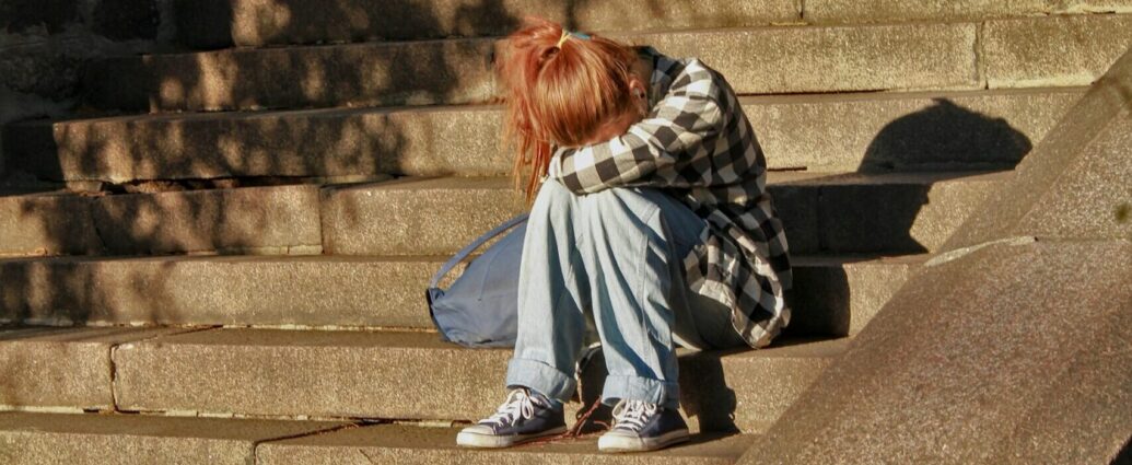 a girl sitting with her head in her lap on concrete stairs.