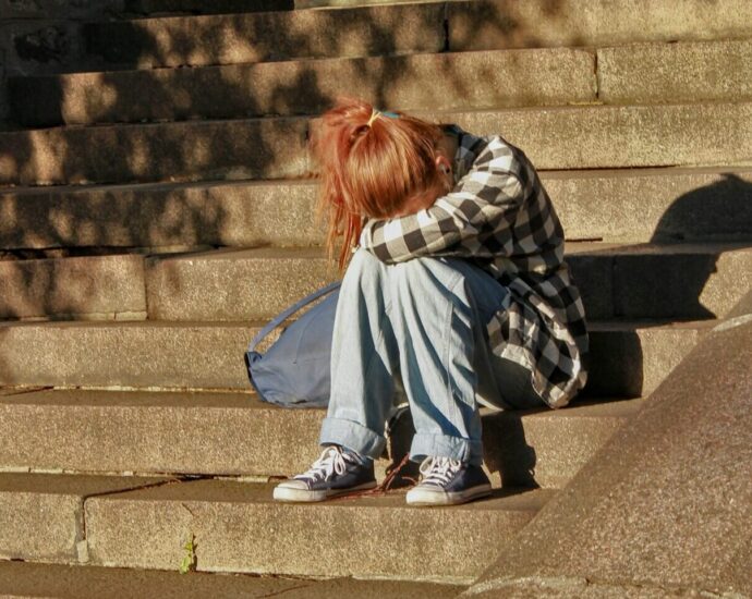 a girl sitting with her head in her lap on concrete stairs.