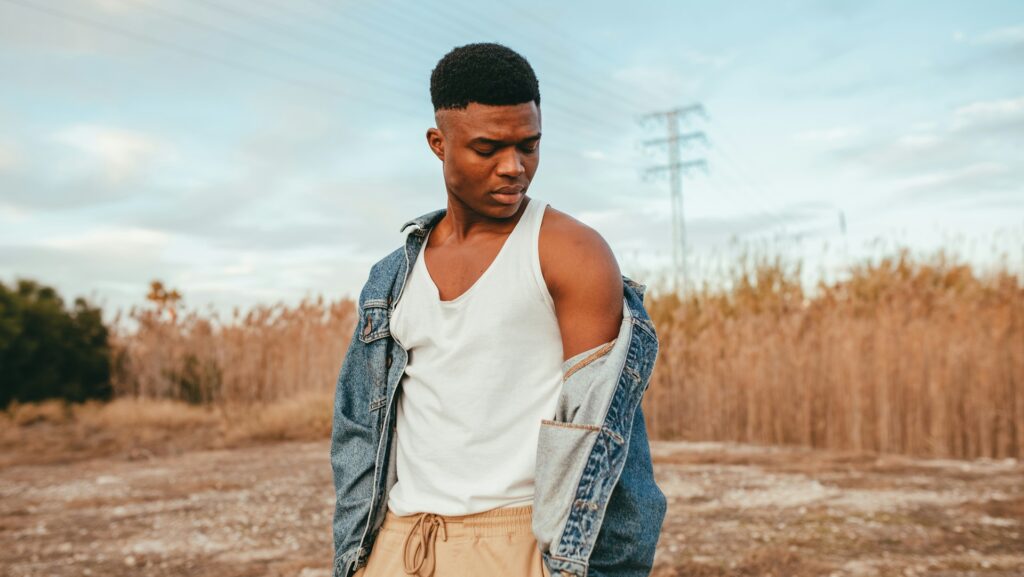 a man dressed in white vest and denim jacket standing in desert-like scenery