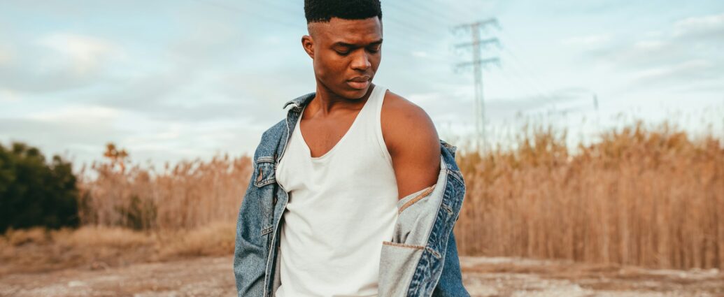 a man dressed in white vest and denim jacket standing in desert-like scenery