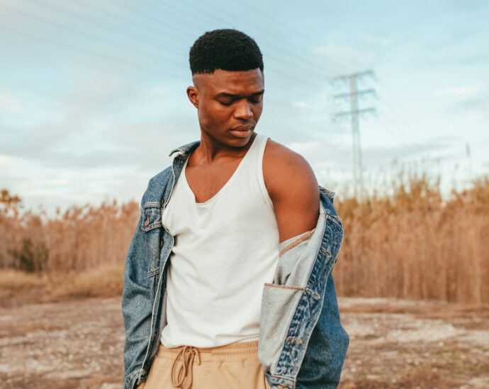 a man dressed in white vest and denim jacket standing in desert-like scenery