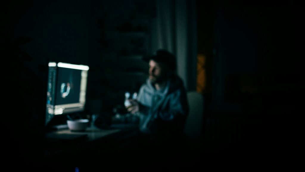 Man in dark room sitting at desk looking at glowing computer screen