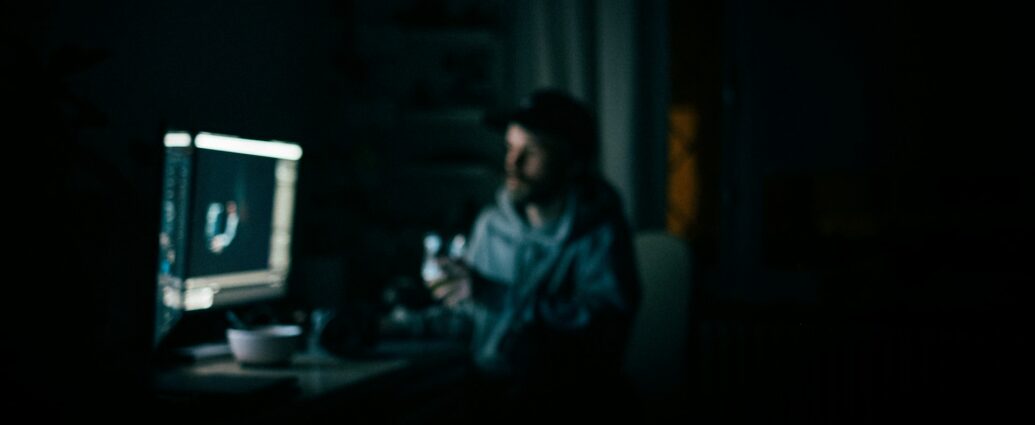 Man in dark room sitting at desk looking at glowing computer screen