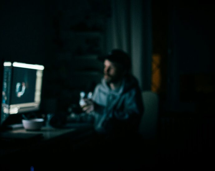 Man in dark room sitting at desk looking at glowing computer screen