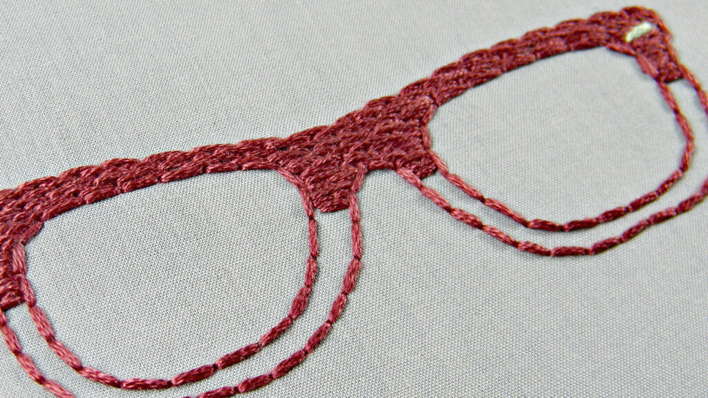 a pair of red wide-rimmed eye glasses are embroidered onto a grey surface.