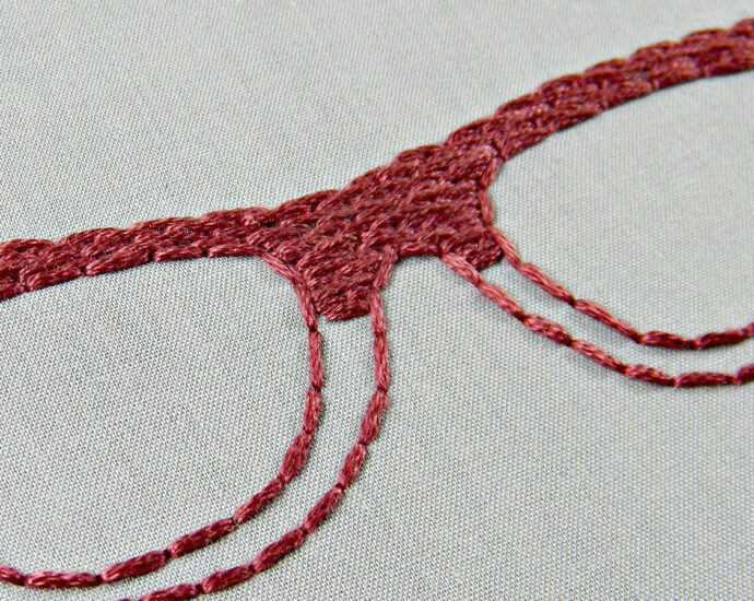 a pair of red wide-rimmed eye glasses are embroidered onto a grey surface.