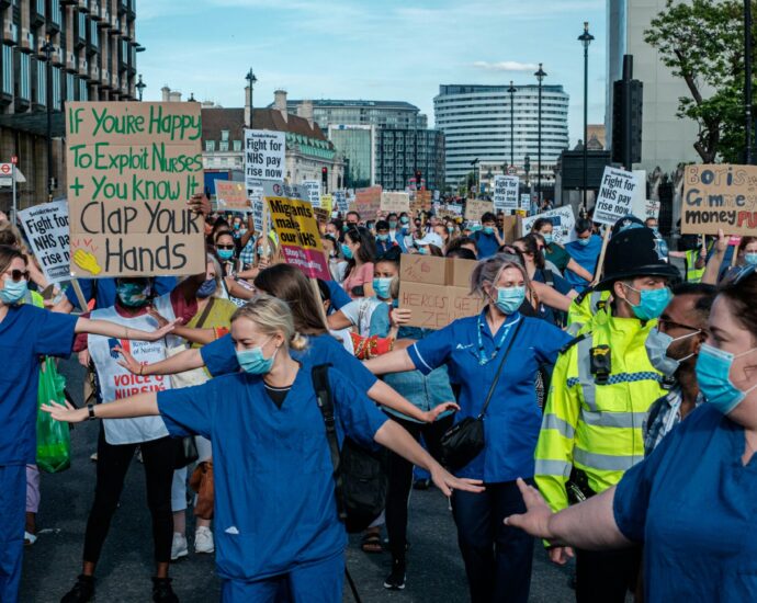 Nurses in blue scrubs and face masks standing with their arms outstretched in the middle of the road during NHS strikes