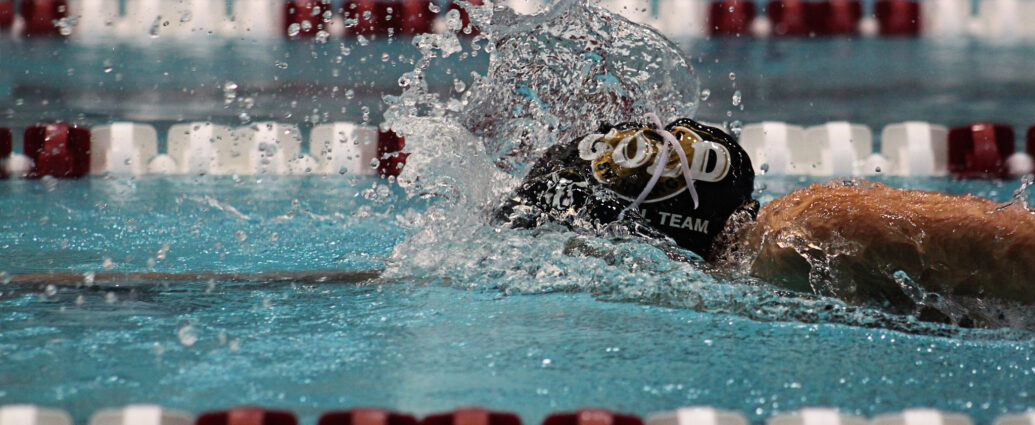 A person wearing a black swimming cap making a splash as they swim along a swimming pool lane alongside red and white floating markers. Achieng Ajulu-Bushell