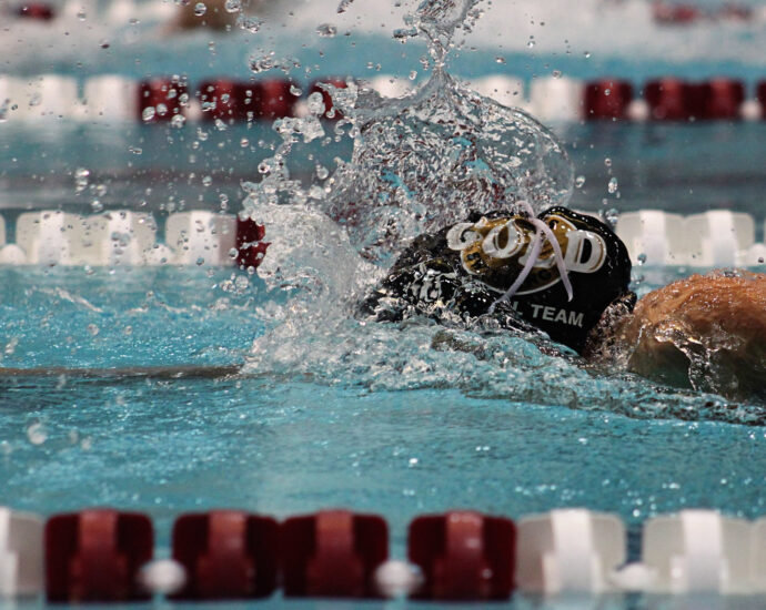 A person wearing a black swimming cap making a splash as they swim along a swimming pool lane alongside red and white floating markers. Achieng Ajulu-Bushell