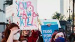 A group of people holding up signs about transgender women's rights and wearing masks.