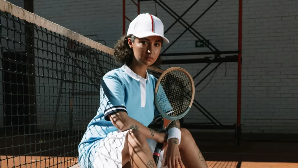 A stylist woman wearing a blue shirt, white cap and white shorts, sat holding tennis racket