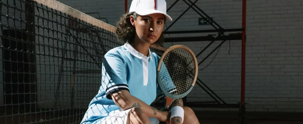 A stylist woman wearing a blue shirt, white cap and white shorts, sat holding tennis racket