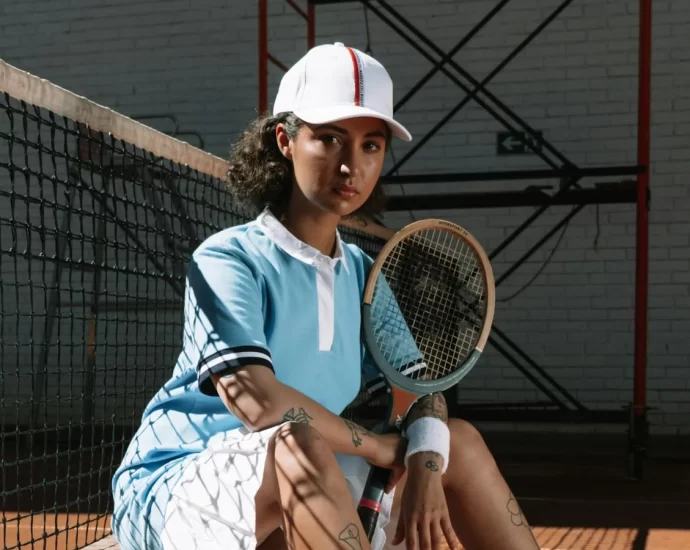 A stylist woman wearing a blue shirt, white cap and white shorts, sat holding tennis racket