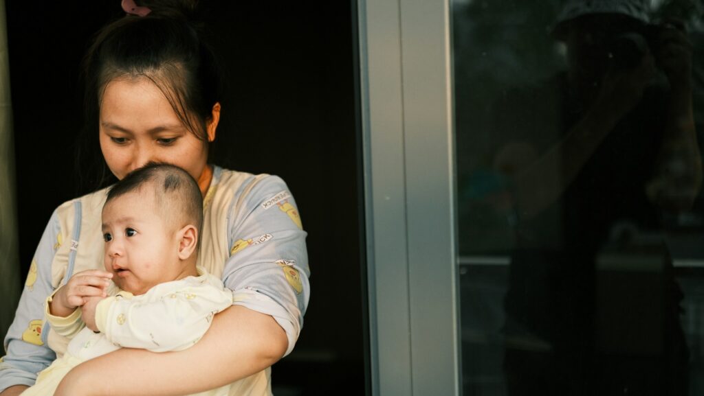 A woman holding a baby in her arms, kissing the baby's head.