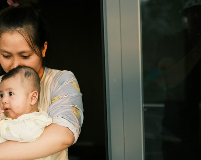 A woman holding a baby in her arms, kissing the baby's head.