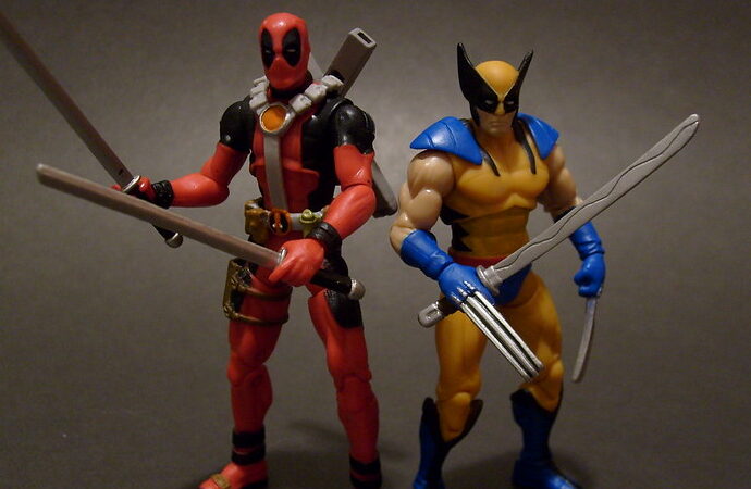 Deadpool & Wolverine figures. Action men figures one is red and navy, the other is yellow and blue, holding swords.