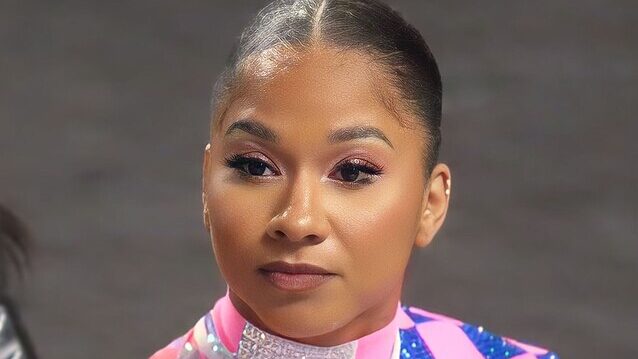 Jordan Chiles wearing pink and navy sequin gymnast costume with slicked back hair in a bun.