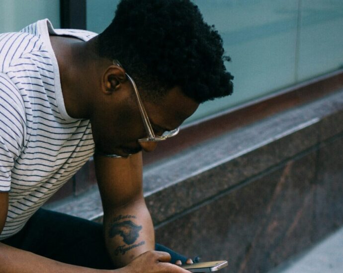 a black man sitting leaning over his mobile phone, reading reclaimed slurs.