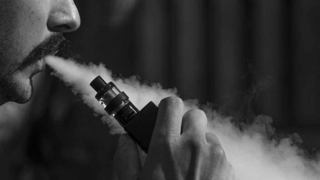 Black and white image of a man blowing smoke from a vape.