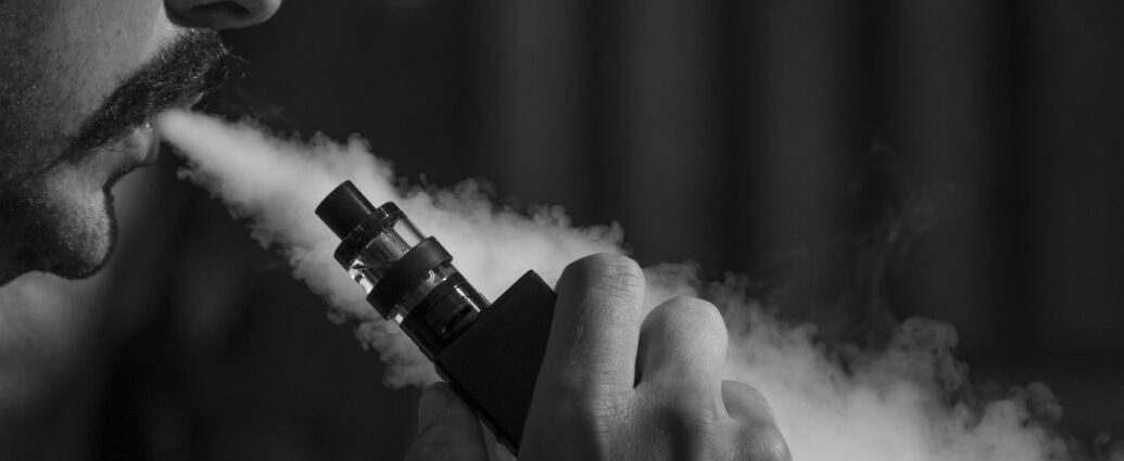 Black and white image of a man blowing smoke from a vape.