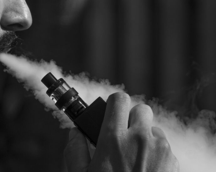 Black and white image of a man blowing smoke from a vape.