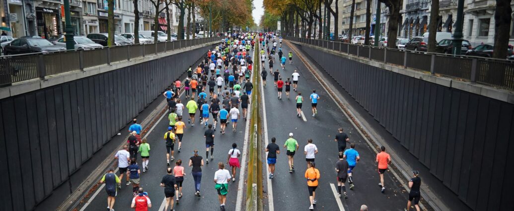 Runners in brightly coloured tops running up a road lined by trees as part of a Marathon event