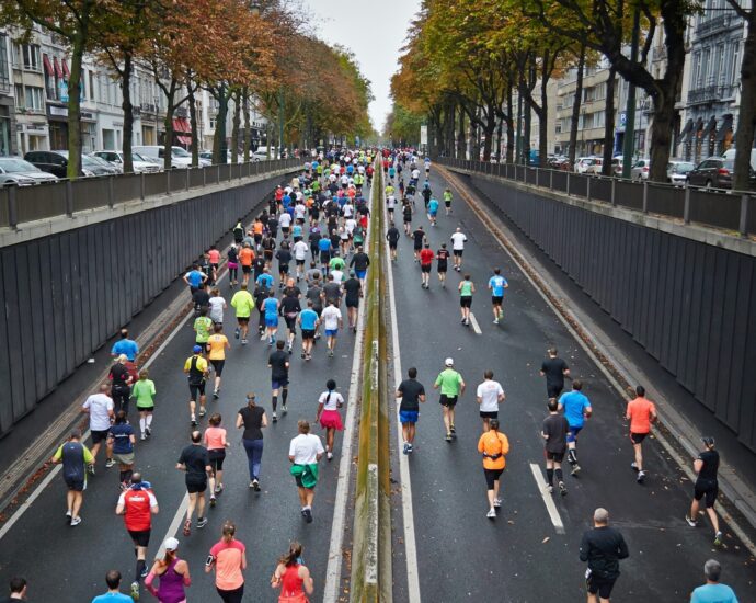 Runners in brightly coloured tops running up a road lined by trees as part of a Marathon event