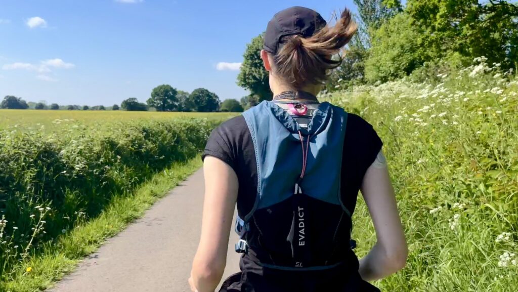 The back of a girl running with her hair in a ponytail, wearing a running vest as she tries Chi Running.