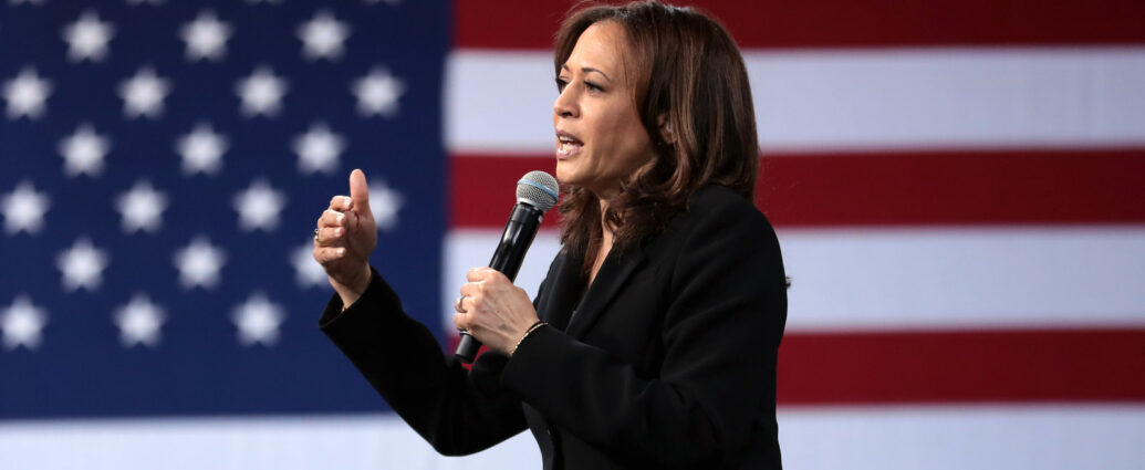 Kamala Harris speaking into microphone in front of USA flag.