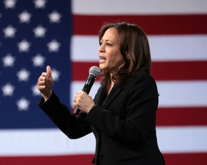 Kamala Harris speaking into microphone in front of USA flag.