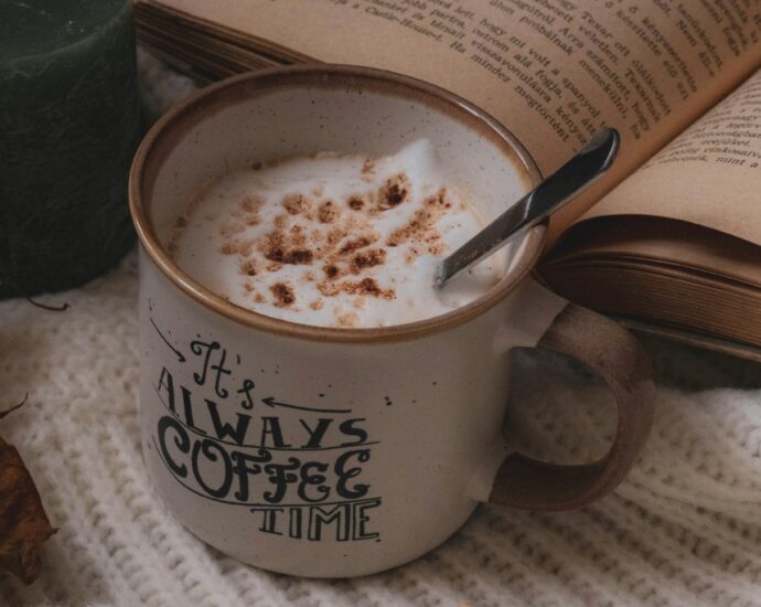 a mug of frothy coffee next to book on cream blanket.