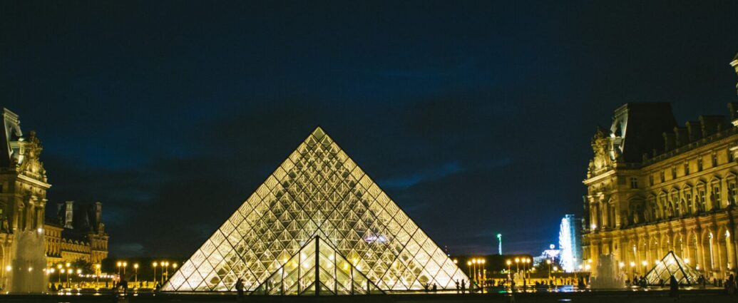 Image of triangular Louvre in Paris lit up in dark. Thousands of people protest in support of Gisèle Pelicot.