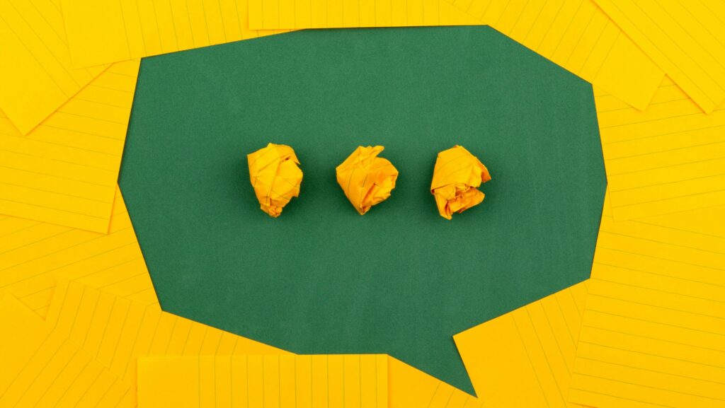 A speech bubble cut out of green paper, with three dots made from scrunched up yellow paper, indicating someone is about to talk in the MLE dialect.