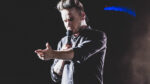 Liam Payne with arm outstretched and microphone in other hand singing on stage