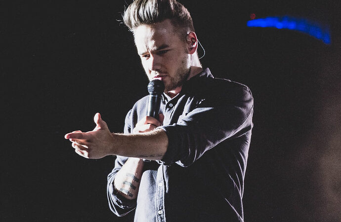 Liam Payne with arm outstretched and microphone in other hand singing on stage