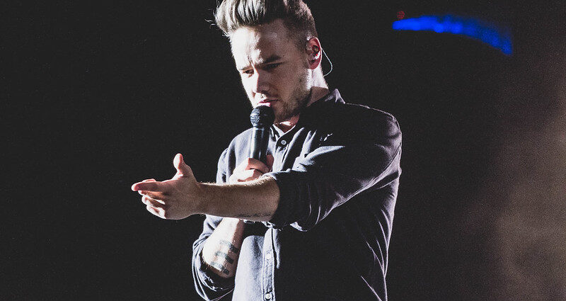 Liam Payne with arm outstretched and microphone in other hand singing on stage