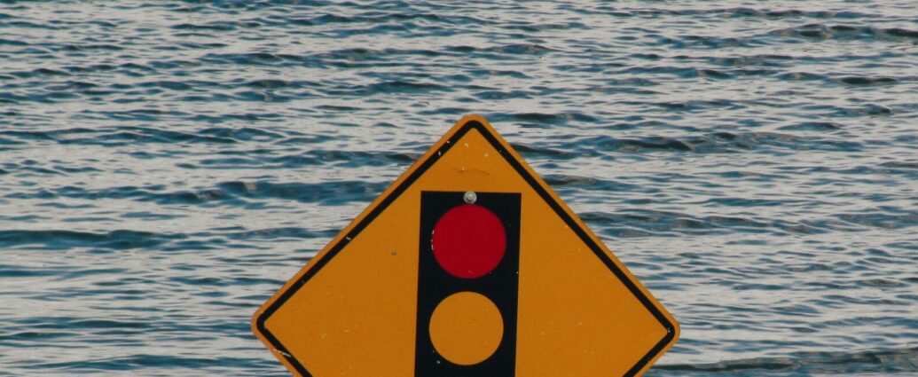 Red, amber and green traffic light symbol on yellow diamond sign sinking in water.