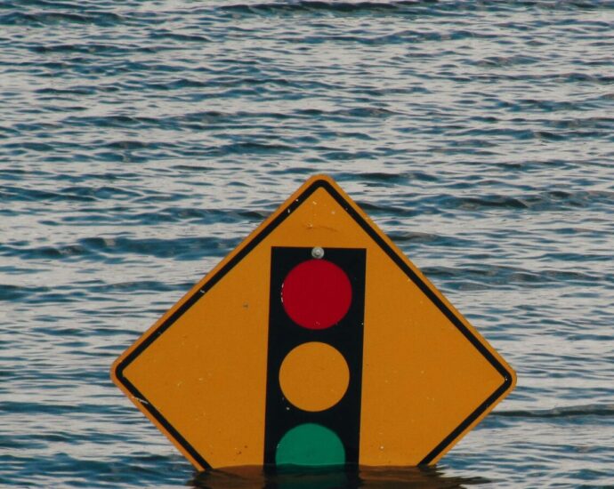 Red, amber and green traffic light symbol on yellow diamond sign sinking in water.