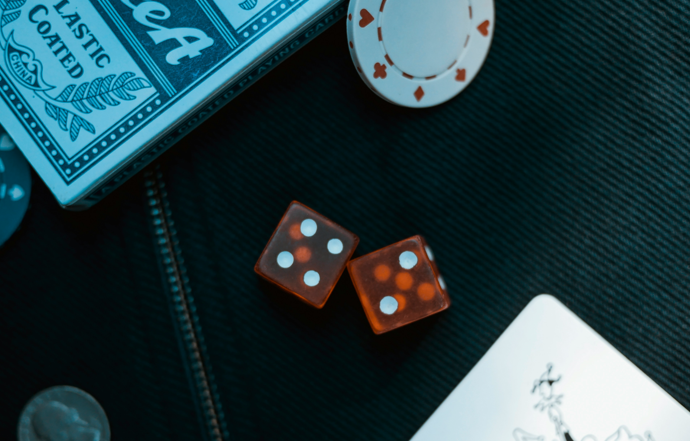 Two orange dice on black surface with poker coin representing Joker: Folie á Deux