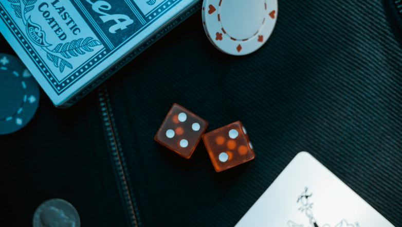 Two orange dice on black surface with poker coin representing Joker: Folie á Deux