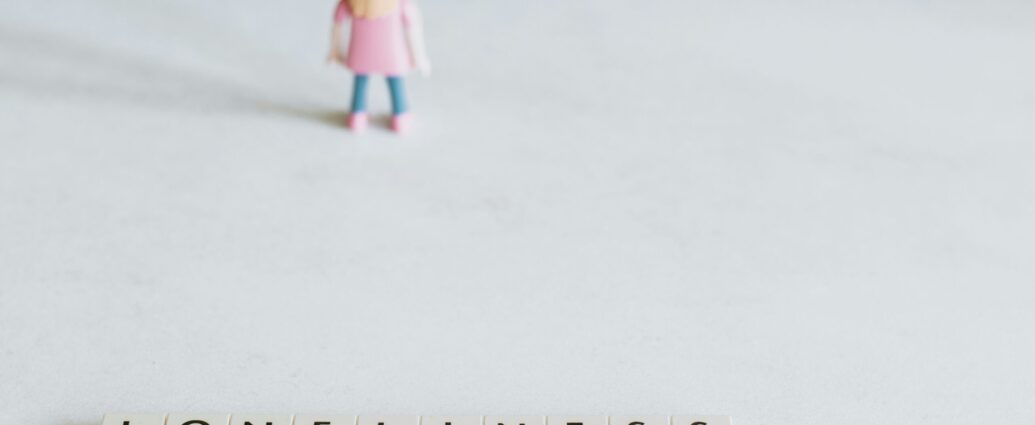 A girl figurine in pink top and blue trousers next to scrabble letters spelling loneliness.