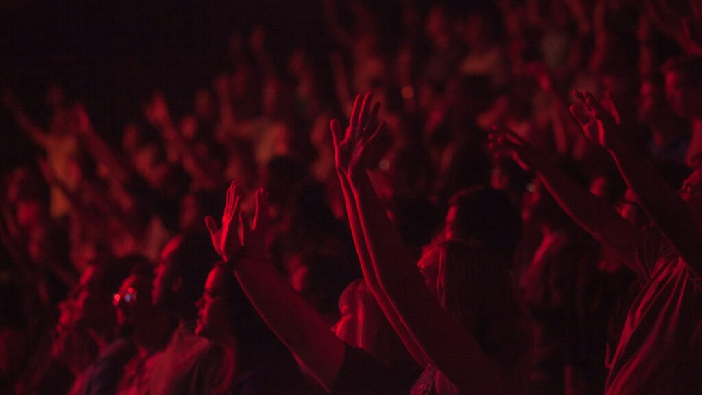 A crowd with arms raised at chappell roan concert with red lighting