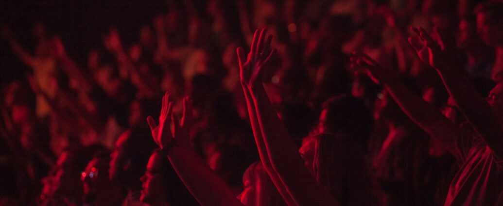 A crowd with arms raised at chappell roan concert with red lighting