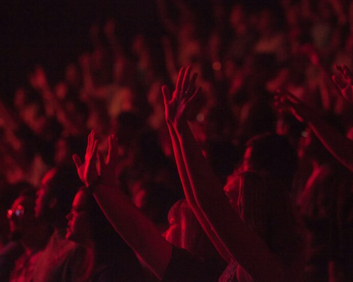 A crowd with arms raised at chappell roan concert with red lighting