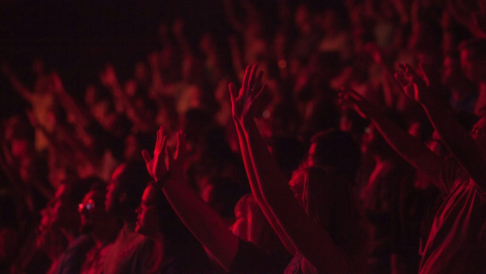 A crowd with arms raised at chappell roan concert with red lighting