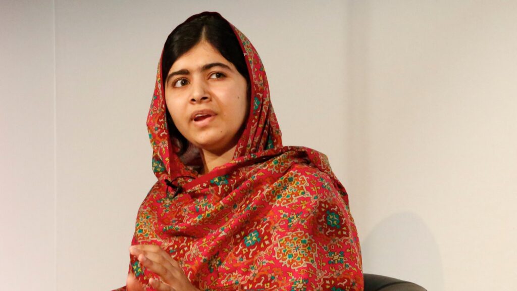 Photo of Malala Yousafzai sitting in a chair, looking off to the side, wearing a red and green patterned dupatta